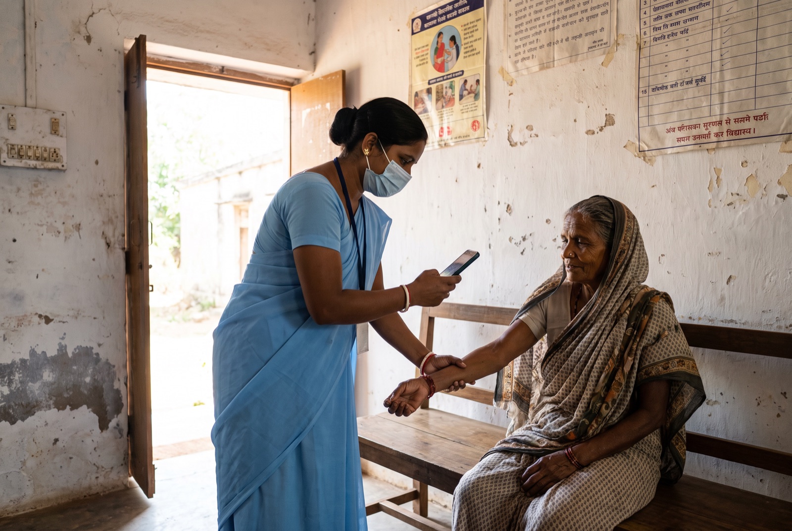A community health worker photographs an older patient's forearm with a phone at a rural health center in India